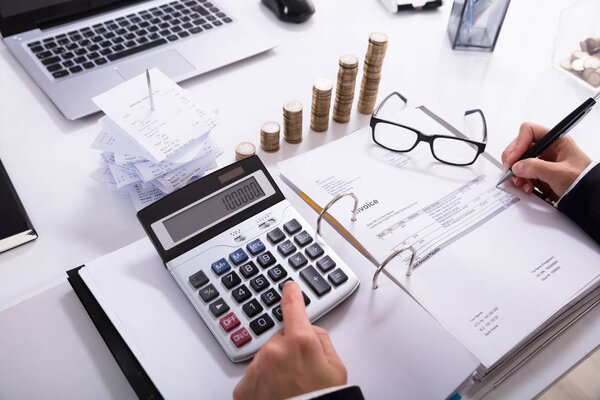 Упакованные монеты и ноутбук перед предпринимательницей Расчет счета-фактуры с помощью калькулятора в офисе
