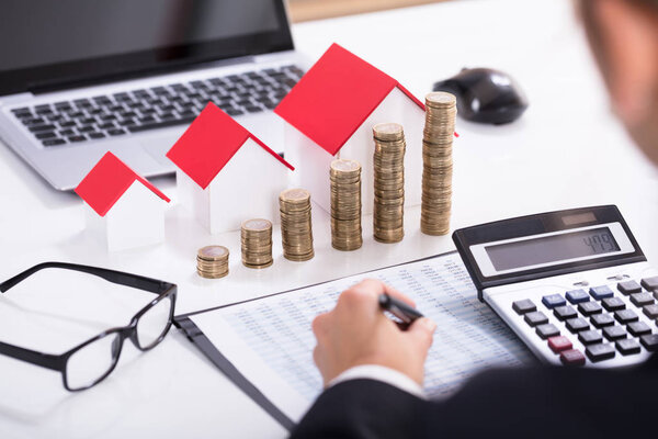 Предприниматель рассчитывает налог перед моделями домов и сложенными монетами с очками и калькулятором
