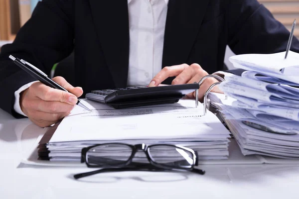 Midsection Of Businessperson Calculating Invoice With Calculator And Bills On Desk