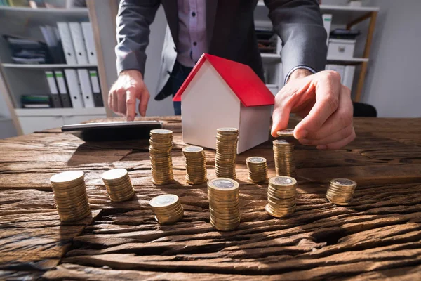 生意人的手的关闭计数堆积硬币与房子模型在木桌 — 图库照片