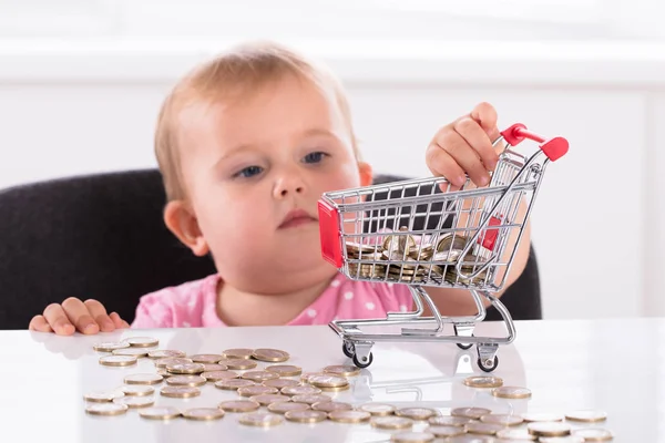 Cute Little Baby Girl Carrying Coin In Shopping Trolley On Desk