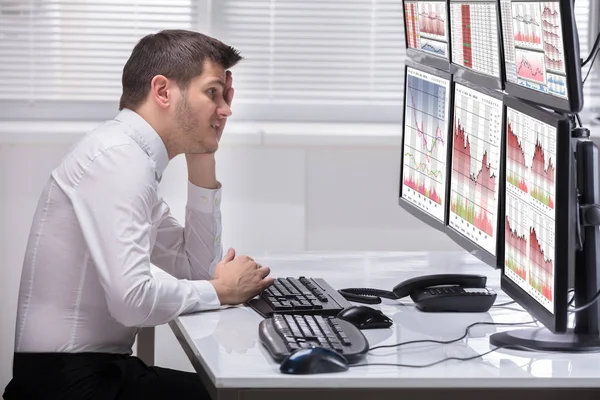 一个有压力的年轻男性操作员的侧面视图在多个计算机屏幕上查看图 — 图库照片