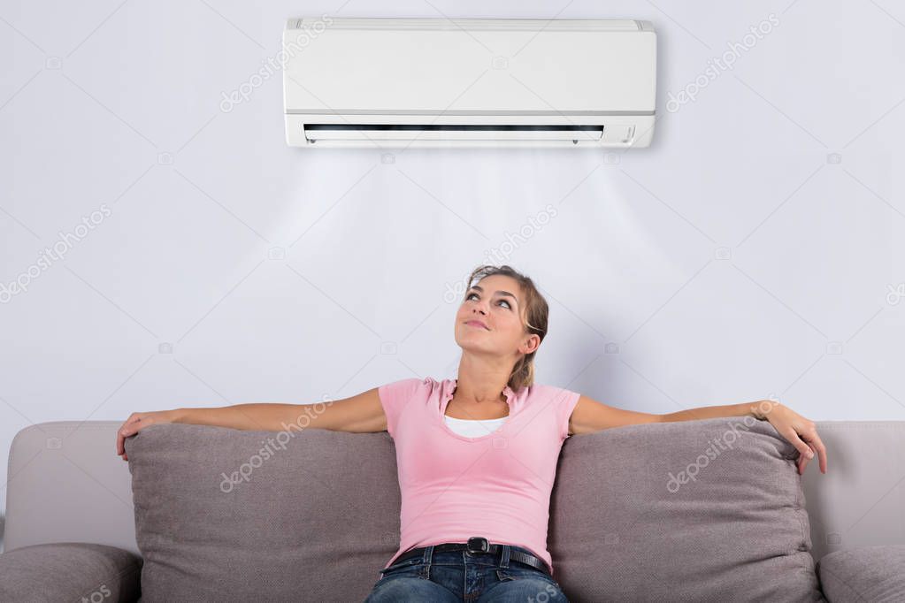 Happy Young Woman Holding Remote Control Relaxing Under The Air Conditioner