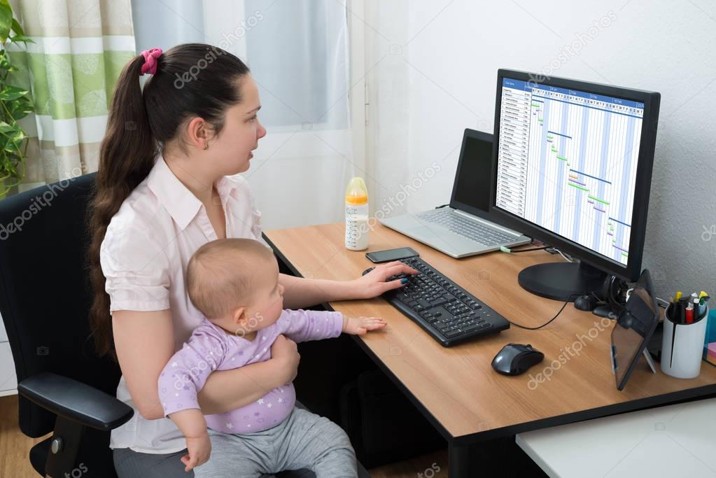 Mid Adult Woman With Baby Girl Looking At Gantt Chart On Computer