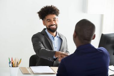 Smiling Young Businessman Shaking Hand With Male Candidate In Office clipart