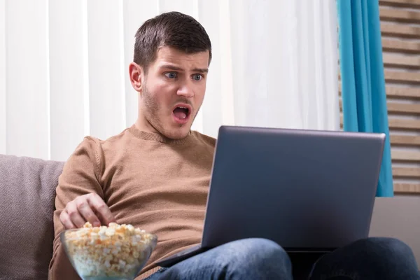 Šokovaný Muž Dívá Laptop Jíst Popcorn Doma — Stock fotografie