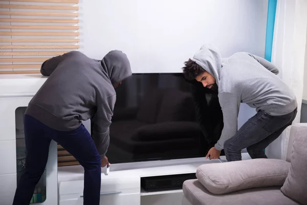 两名男性劫匪在蒙面顶部举起电视在起居室里 — 图库照片