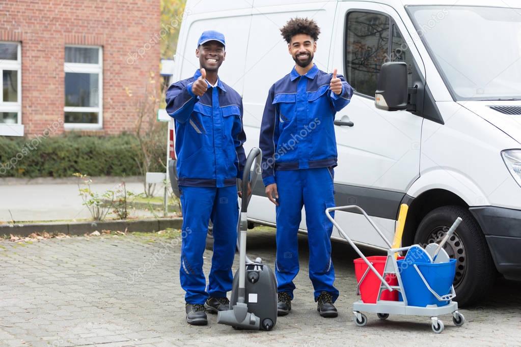 Portrait Of Two Happy Male Janitor Standing With Cleaning Equipment Against Truck