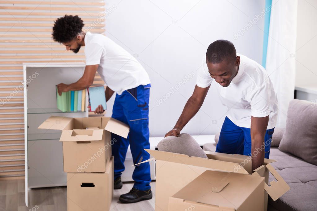 Two Young Movers Placing The Books In The Shelf From The Cardboard Boxes