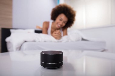 Gülümseyen genç kadın yatakta uzanıyor. Telsiz hoparlörde müzik dinliyor.