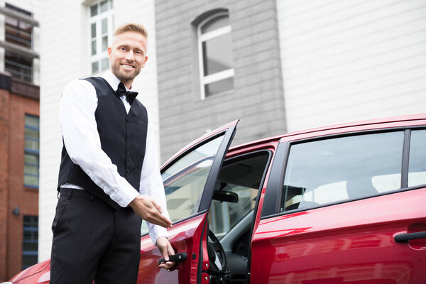 Portrait Of A Handsome Young Male Valet Opening Red Car Door