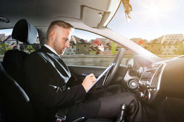 Side View Of A Man Writing On Clipboard Inside Self Driving Car