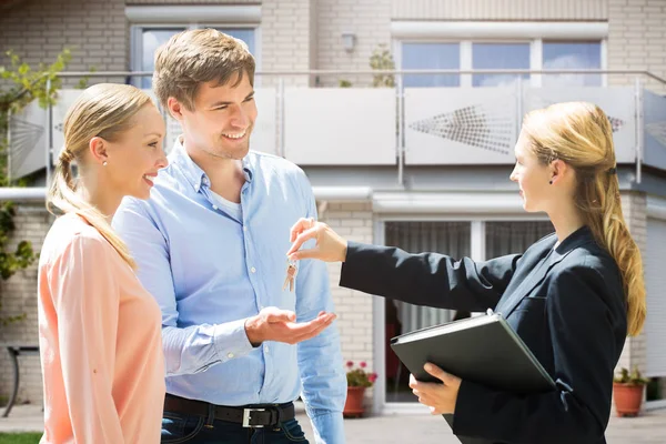 Immobilienmaklerin Gibt Lächelndem Jungen Paar Hausschlüssel — Stockfoto