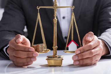 Yığılmış sikke ve ev modeli üzerinde ölçek ağırlığında koruyan bir işadamının'ın el Close-Up