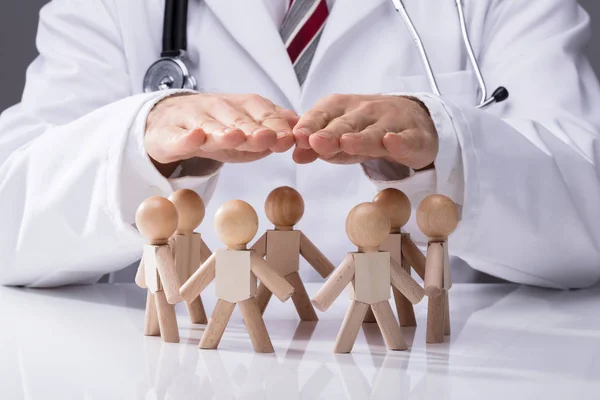 Close Doctor Hand Protecting Wooden Figures Desk — Stock Photo, Image