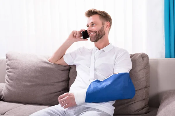 Jovem Com Mão Fraturada Sentado Sofá Conversando Telefone Móvel — Fotografia de Stock