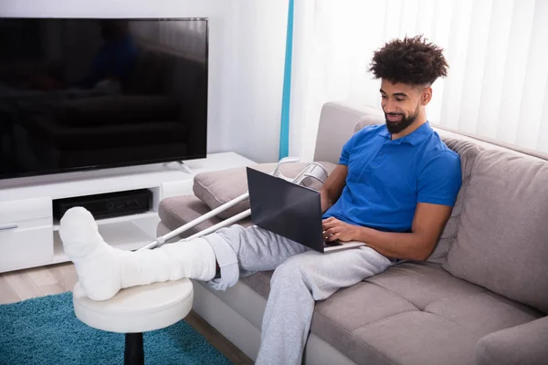 Mężczyzna Złamaną Nogą Siedząc Kanapie Przy Użyciu Laptopa — Zdjęcie stockowe