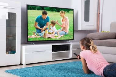 Genç kadın uzaktan tutarak ve evde televizyon izlerken mavi halı üzerinde yalan