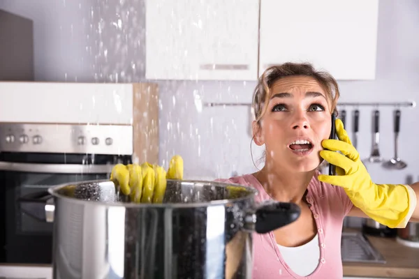 Shocked Woman Calling Plumber While Collecting Water Leaking Ceiling Using — Stock Photo, Image