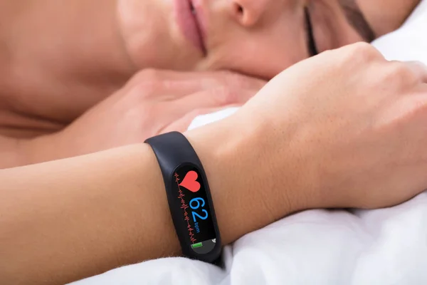 Close-up Of Fitness Activity Tracker With Heartbeat Rate On Woman\'s Hand Over Bed