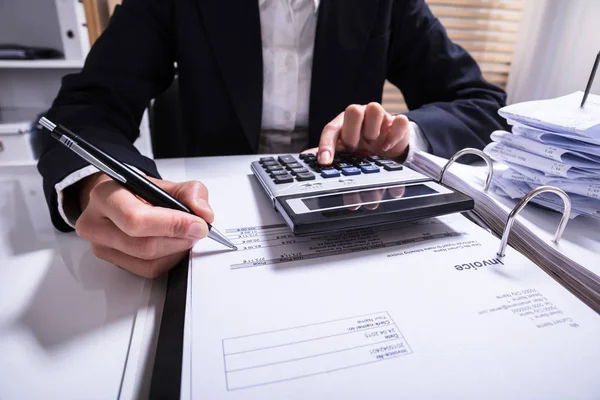 Midsection Of Businessperson Calculating Invoice With Calculator And Bills On Desk