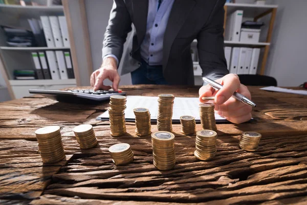 Geschäftsmann Berechnet Gestapelte Goldmünzen Mit Taschenrechner Auf Holztisch — Stockfoto