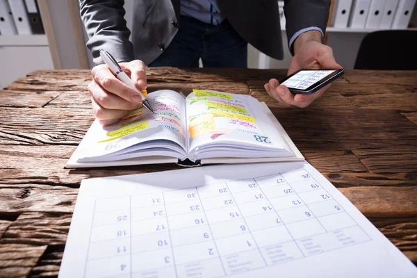 Businessperson Holding Mobile Phone Writing Schedule Diary — Stock Photo, Image
