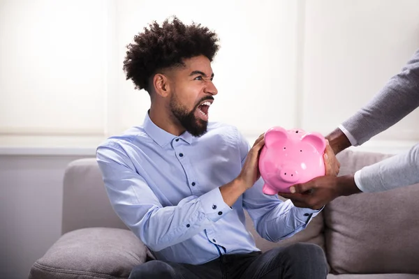 Aggressive Young Man Sitting Sofa Fighting Pink Piggybank — Stock Photo, Image