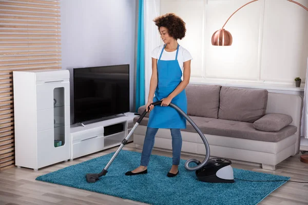 年轻女清洁工在起居室里用吸尘器清扫地毯 — 图库照片