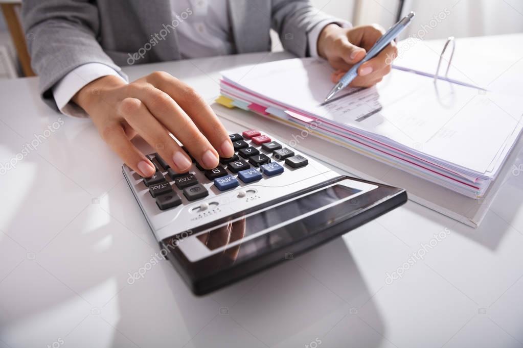 Close-up Of Businessperson Calculating Bills With Calculator In Office