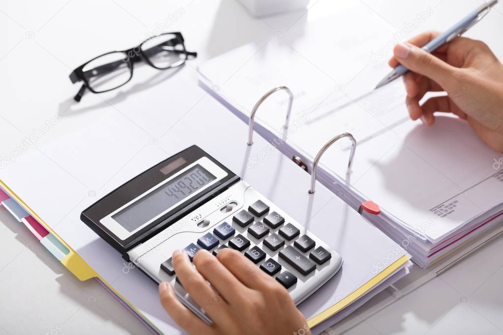 Close-up Of Businessperson Calculating Bills With Calculator In Office