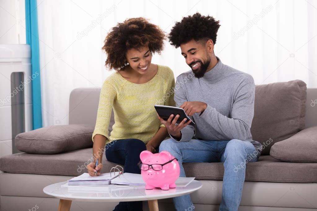 Smiling Young Couple Sitting On Sofa Calculating Invoice