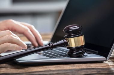 Close-up Of A Businessperson's Hand Using Laptop With Gavel On Wooden Desk clipart