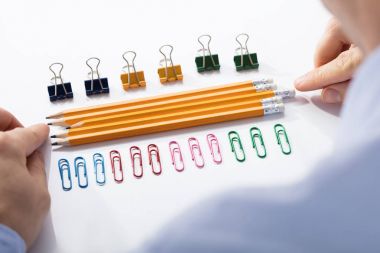 Businessman Arranging The Pencils In Between The Row Of Colorful Pins And Paper Clips clipart
