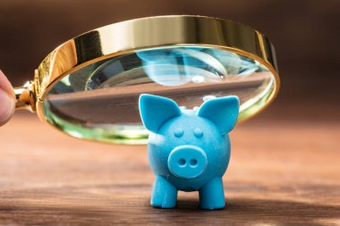 Ahşap masa üzerinde büyüteç ile mavi Piggybank inceleyerek bir kişinin yakın çekim