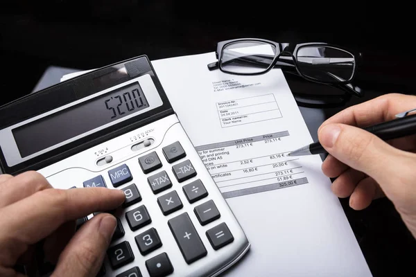 Close-up Of A Businessperson\'s Hand Calculating Invoice With Calculator