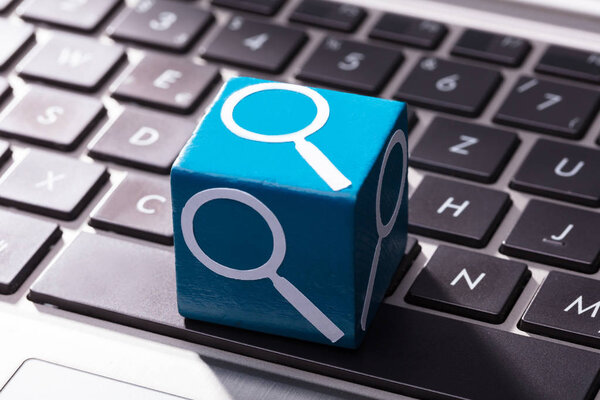 Крупный план увеличительного стекла символа на голубой деревянный блок над ноутбук клавиатуры
