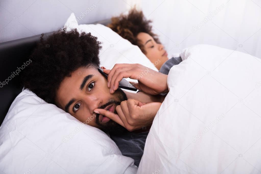 Young Man Talking Privately On Cell Phone While Her Wife Sleeping In Bed