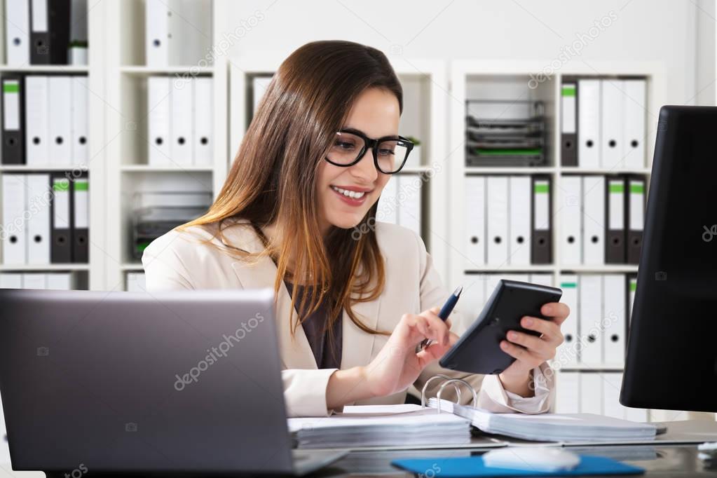 Happy Young Businesswoman Using Calculator At Workplace