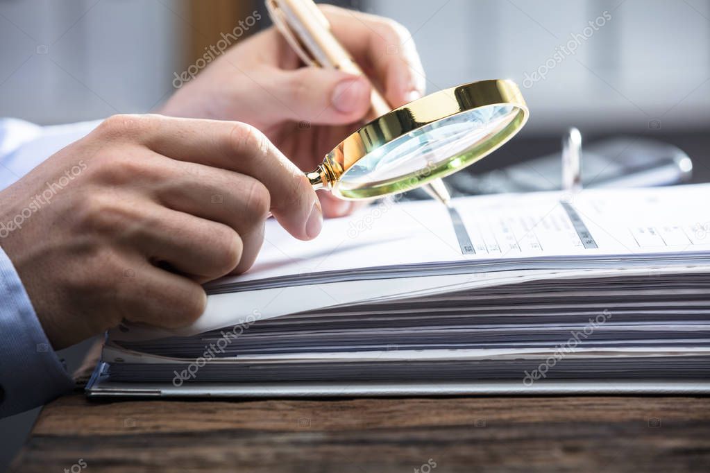 Close-up Of A Businessperson's Hand Looking At Invoice Through Magnifying Glass