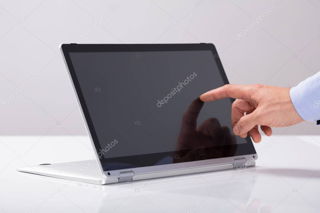 Close-up Of Businessman Touching His Finger On Hybrid Laptop Screen On White Desk