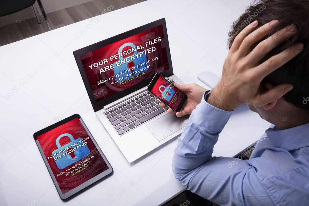 Worried Businessman With Cellphone, Digital Tablet And Laptop With Encrypted Text On The Screen
