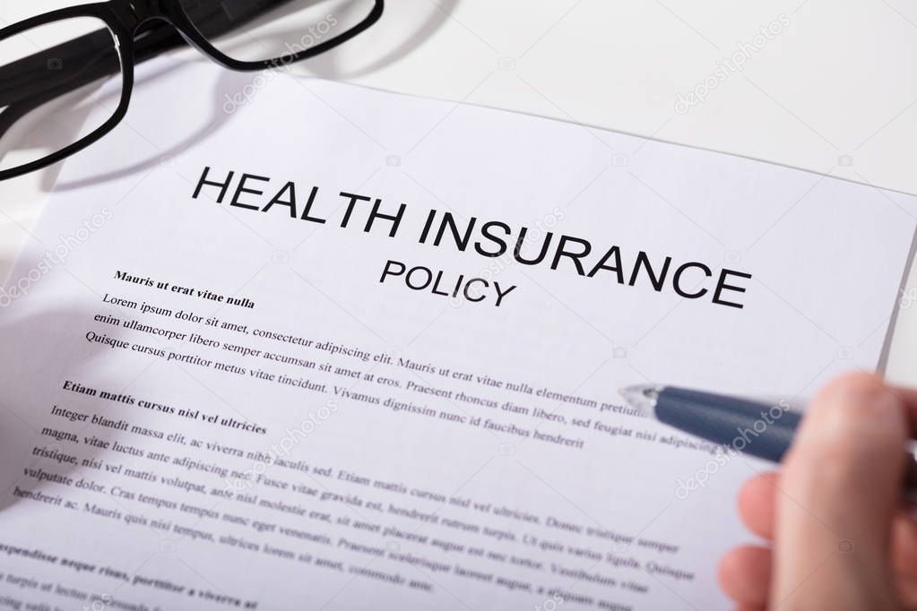 Close-up Of A Person's Hand Holding Pen Over Health Insurance Policy Form