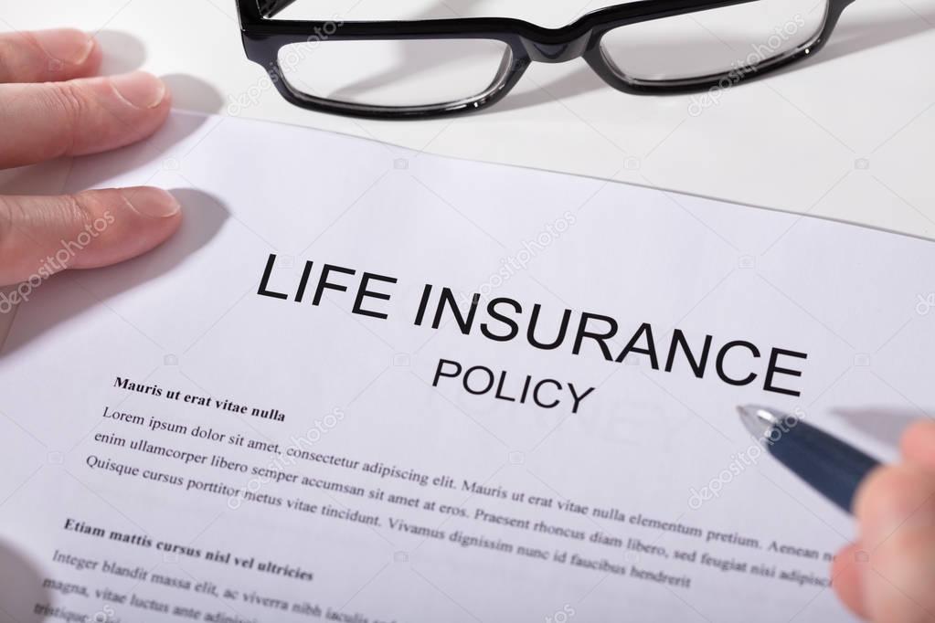 Close-up Of Human Hand Holding Pen Over Life Insurance Policy Form