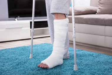 Kırık bacak mavi halı üzerinde yürümek için koltuk değneği kullanarak adamla