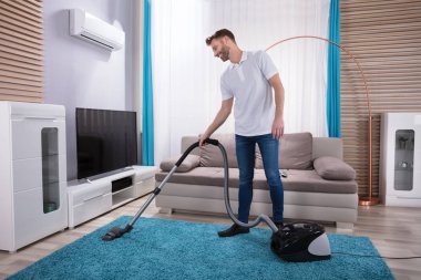 Evde elektrikli süpürge ile temizlik mavi halı genç adam