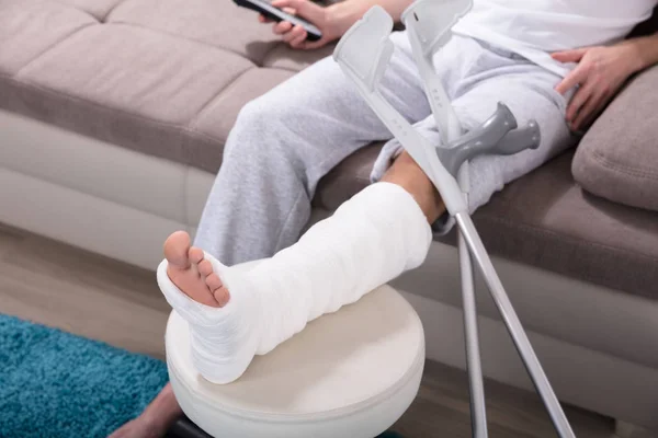 Mladý Muž Zlomenou Nohou Sedí Pohovce Drží Vzdálený — Stock fotografie
