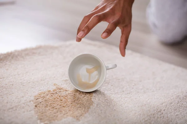 关闭一个人采摘杯溢出咖啡洒在地毯上 — 图库照片