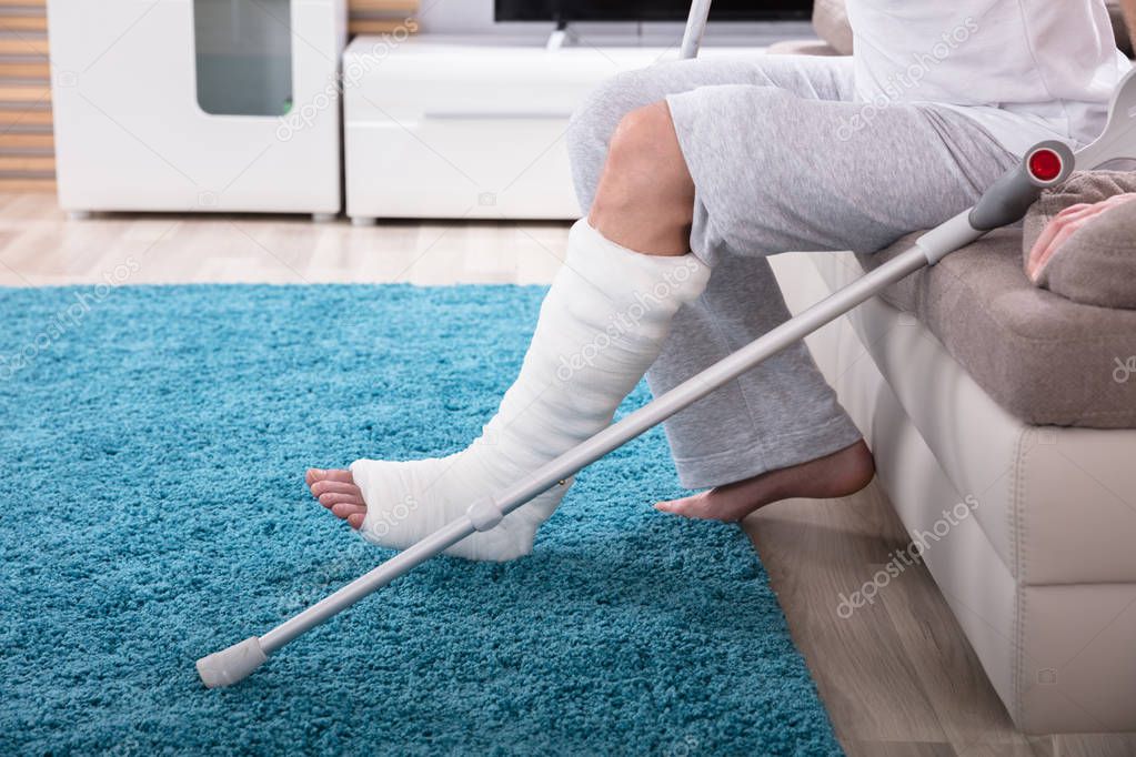 Young Man With Broken Leg Using Crutches To Get Up From Sofa