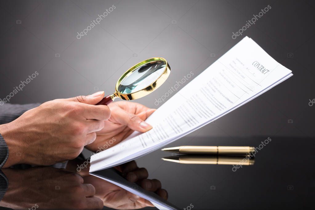 Close-up Of A Judge's Hand Looking At Document With Magnifying Glass